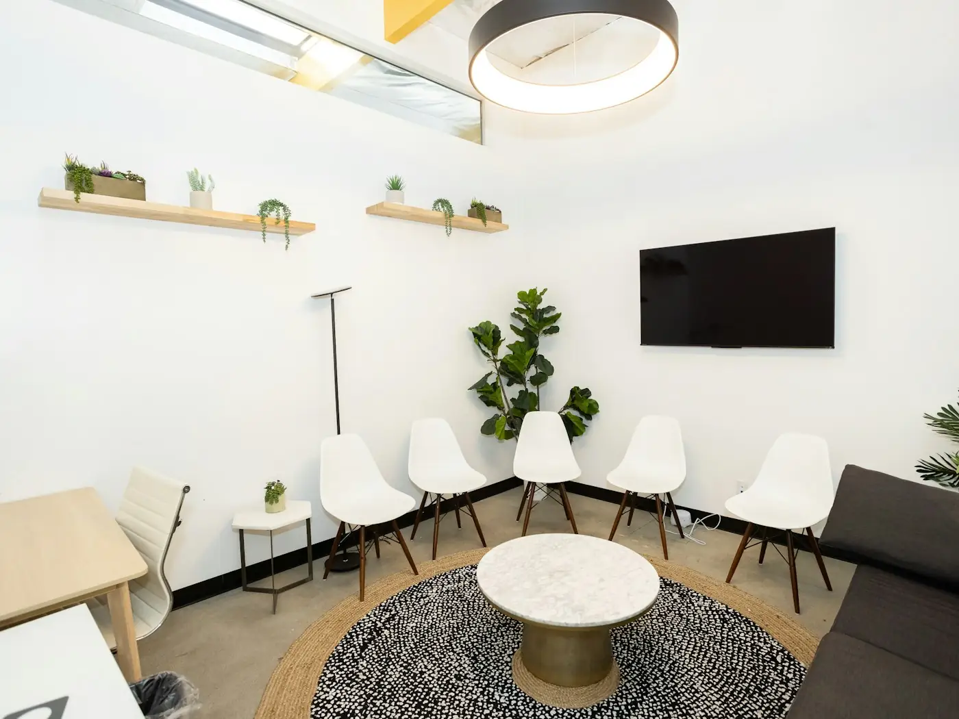 A tidy clinic waiting area with white chairs lined along the wall and potted plants